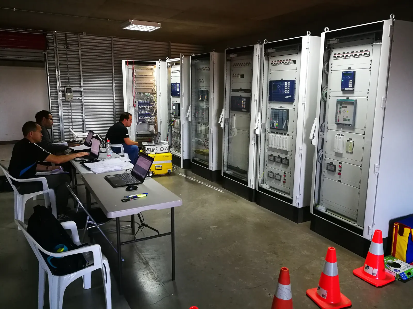 Ingenieros de PAC-E trabajando frente a una fila de tableros de control y protección